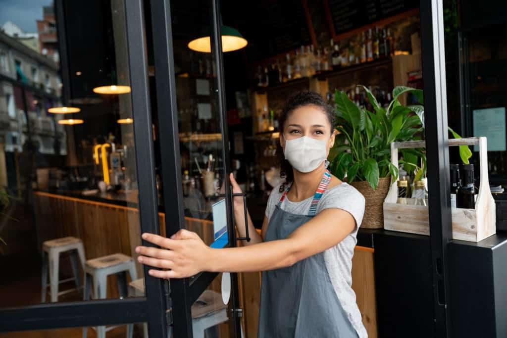 Woman with face mask opening restaurant door